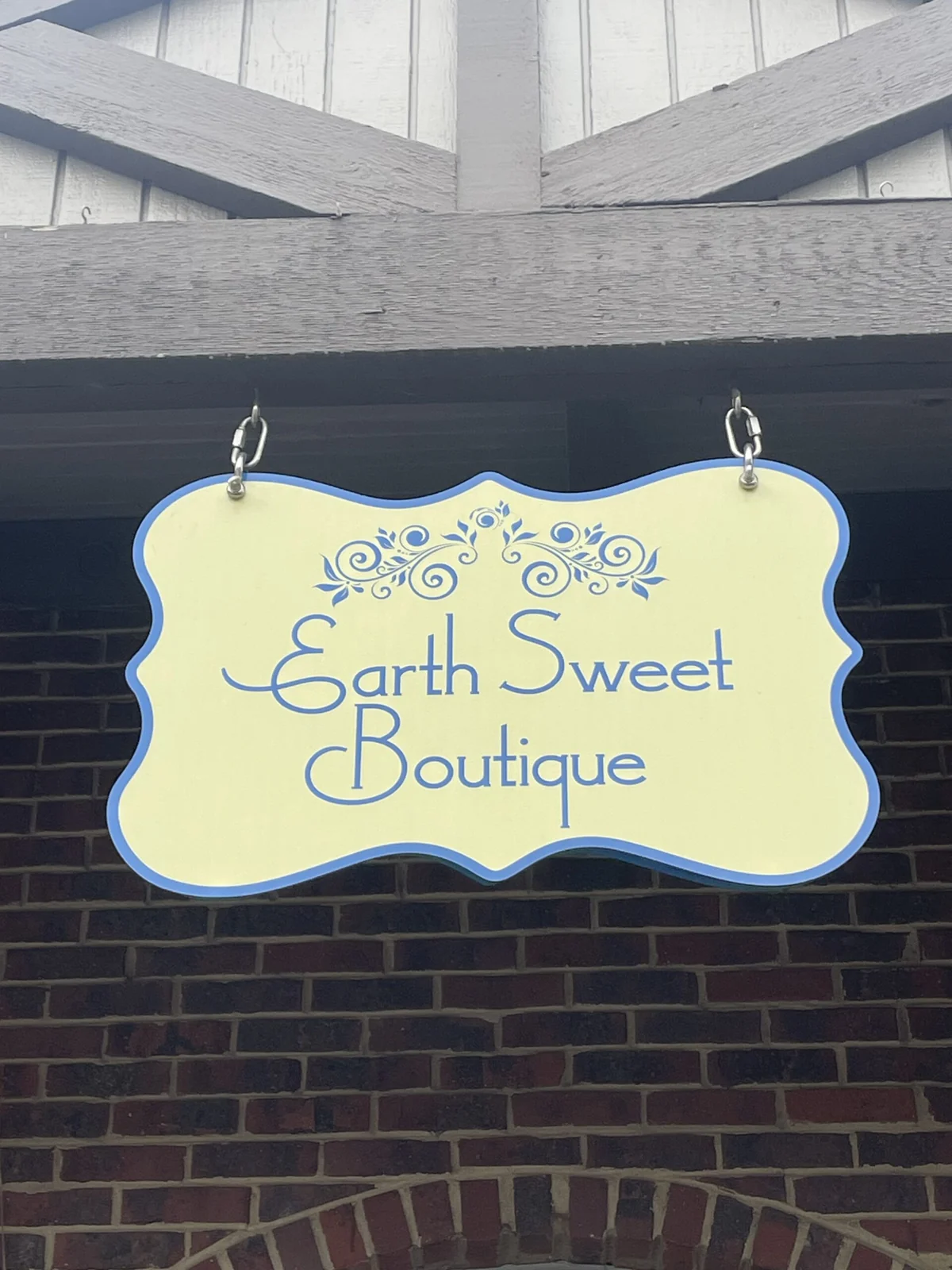 Yellow and blue Earth Sweet Boutique sign hanging outside the brick shop.