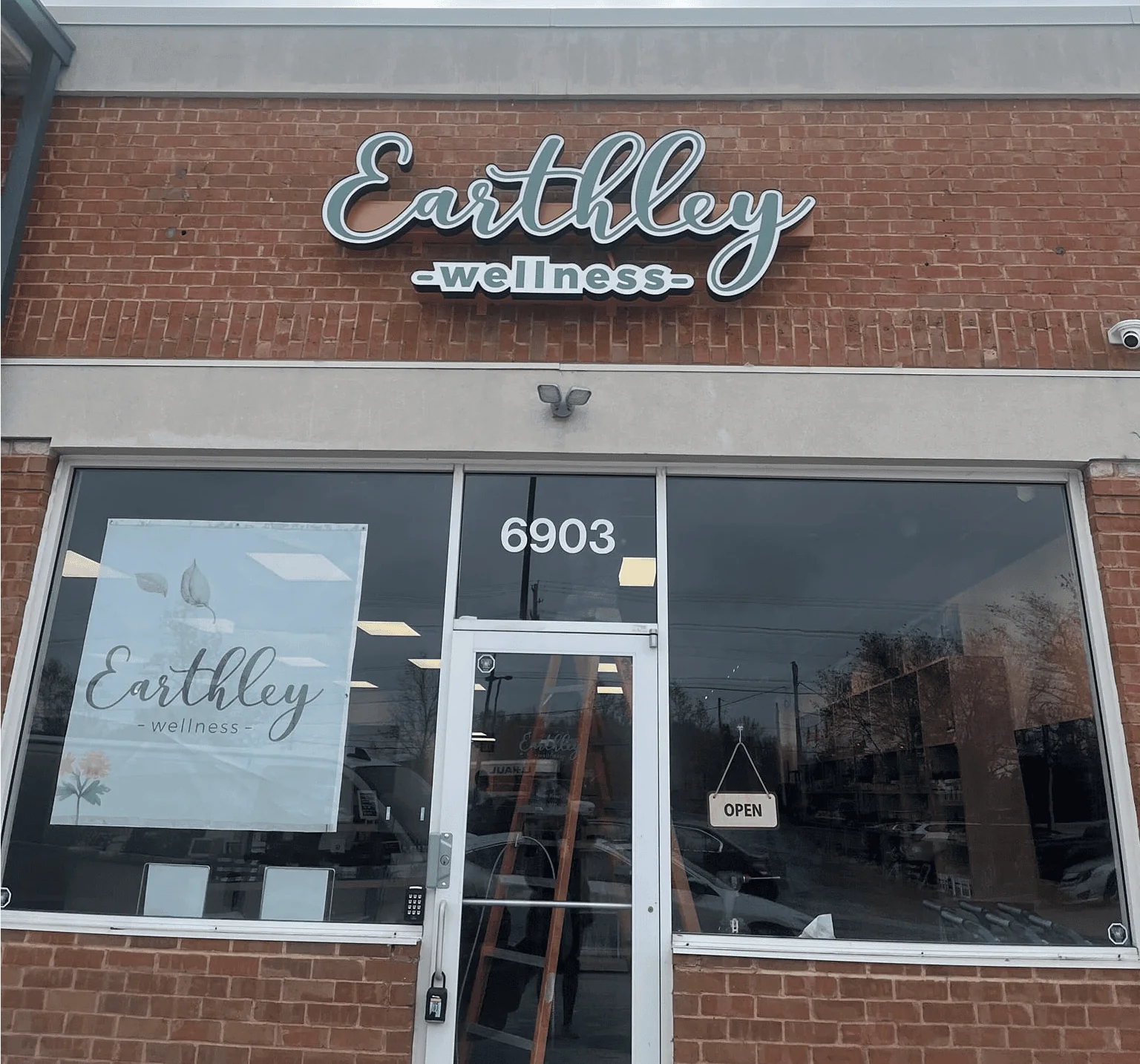 Earthley Wellness retail store exterior showing brick building facade with white Earthley logo sign above large glass storefront windows displaying products at address 6903