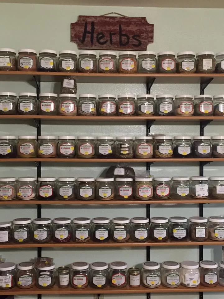 Shelves of labeled bulk herb jars inside The Spice Shack